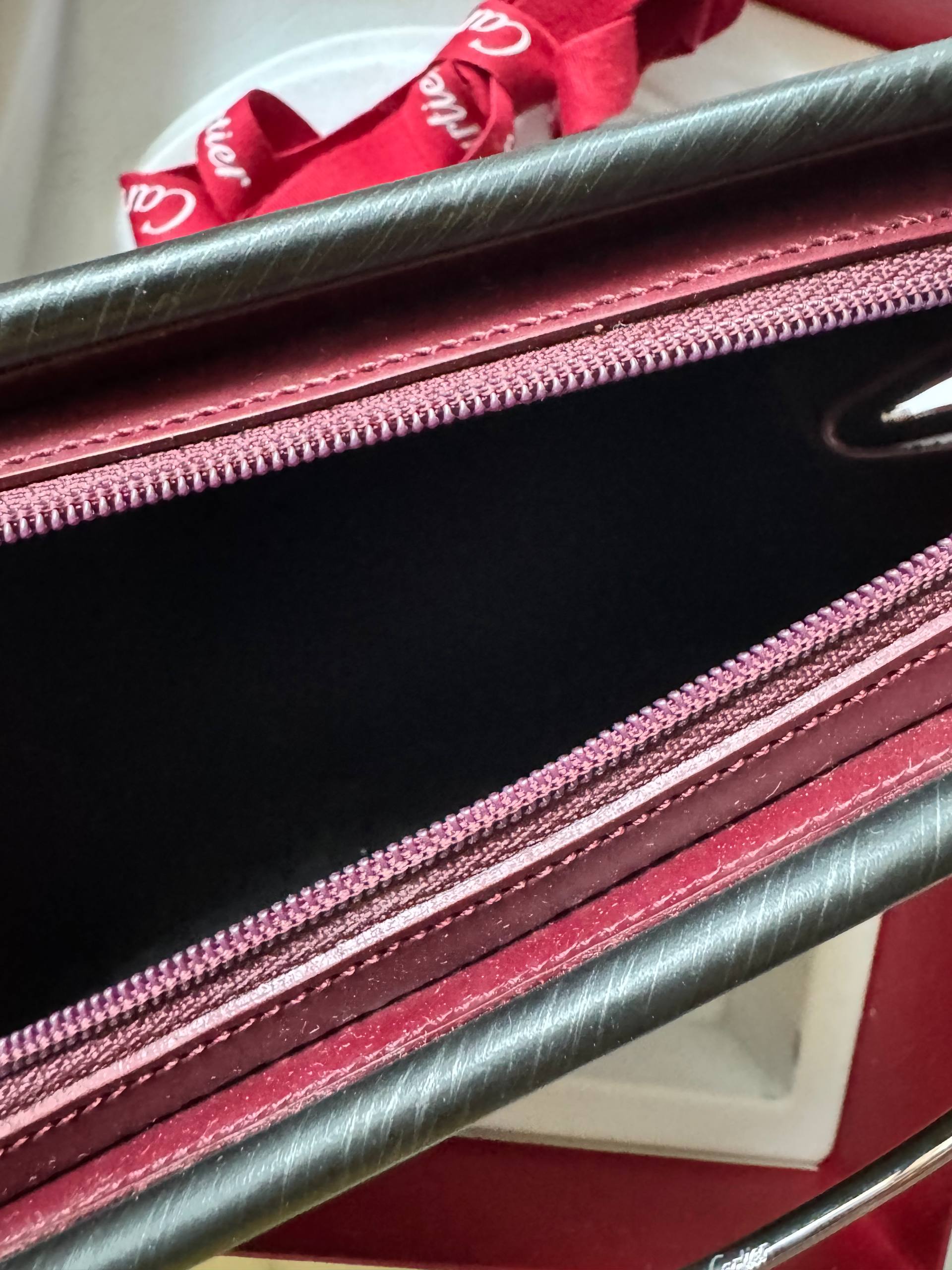Close-up of a red and black Cartier Trinity clutch with a visible brand logo.