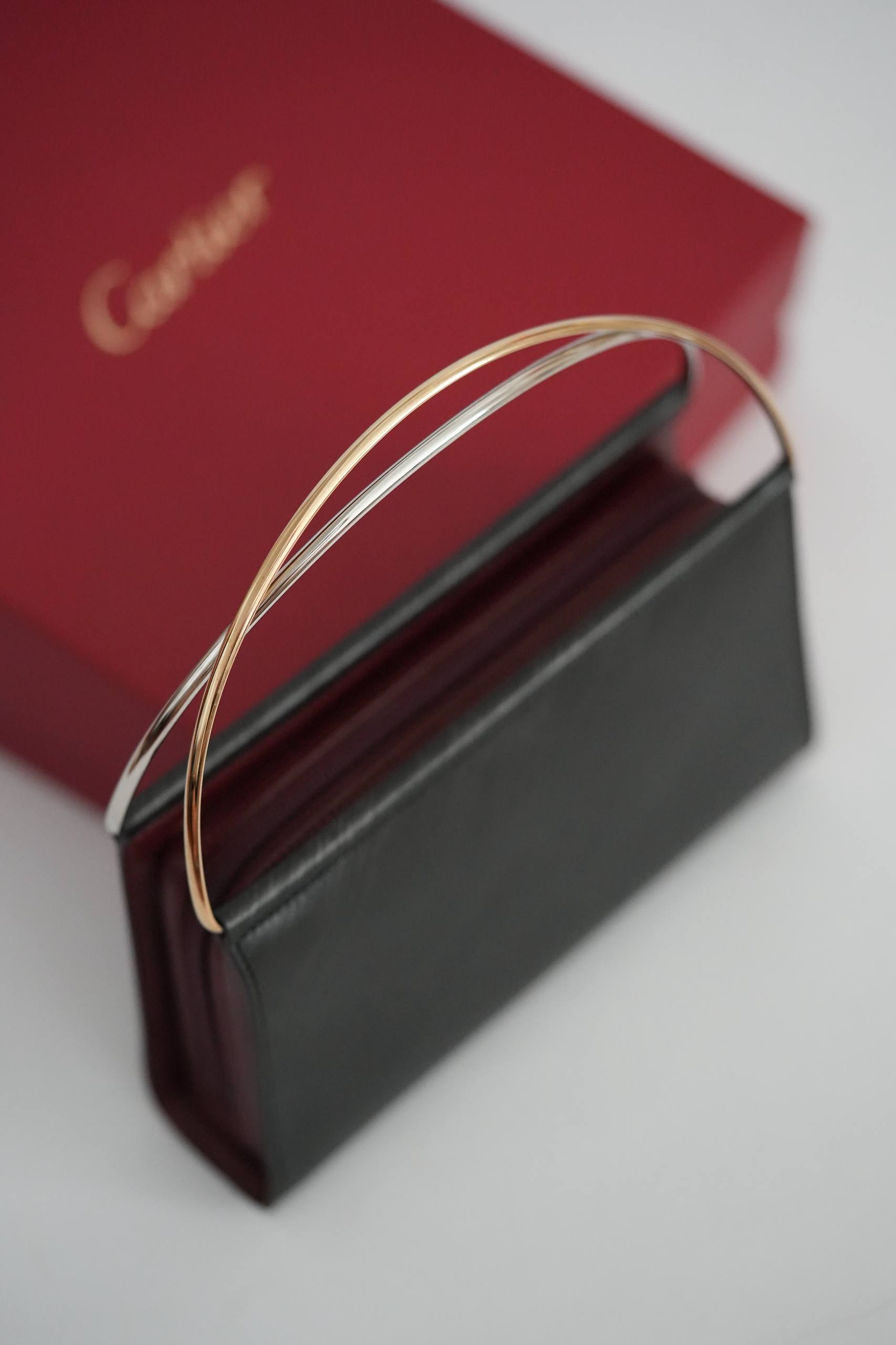 Cartier Trinity top-handle clutch angled view black leather burgundy trim two-tone gold handle