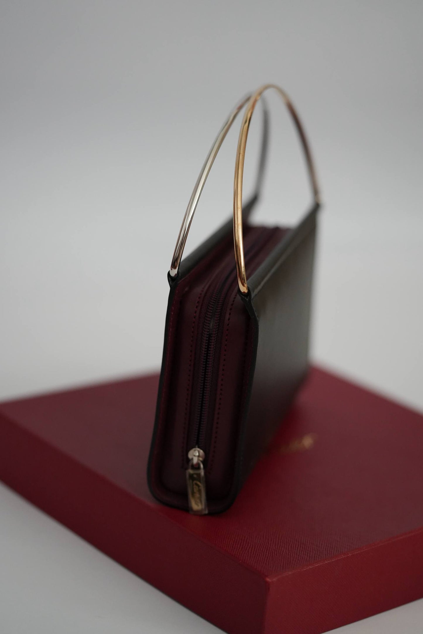 Cartier Trinity clutch side view structured black leather two-tone handle on Cartier red box