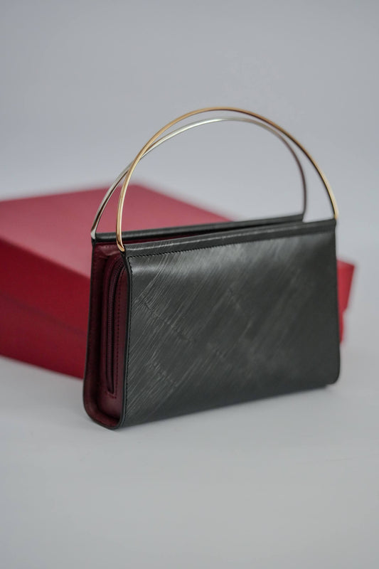 Cartier Trinity top-handle clutch angled view black leather burgundy trim two-tone gold handle with Cartier box behind